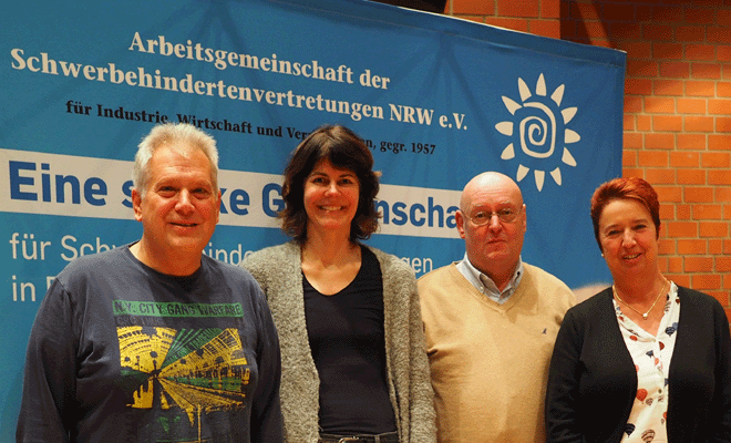 Dreiköpfiger Vorstand der Arbeitsgemeinschaft und BIK-Mitarbeiterin vor Plakatwand