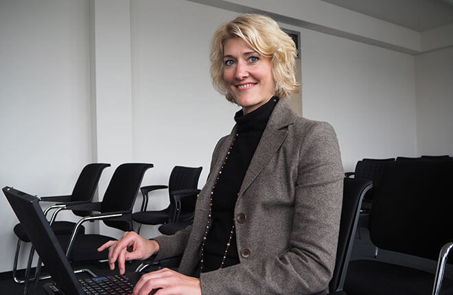 Junge Frau in einem Konferenzraum, auf den Knien ein Laptop