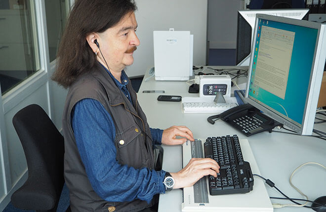 Robbie sitzt an seinem Computerarbeitsplatz mit Braillezeile und Sprachausgabe